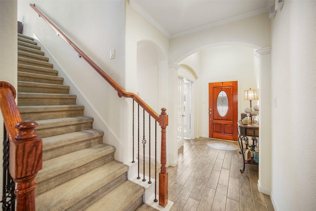 entrance foyer featuring arched walkways, crown molding, stairs, light wood-style floors, and baseboards
