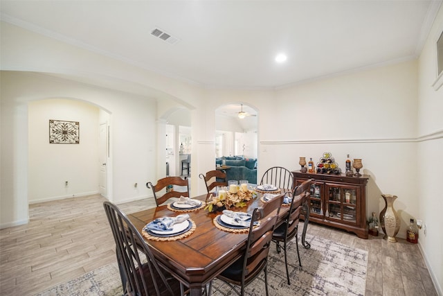 dining area with arched walkways, light wood finished floors, ornamental molding, and baseboards