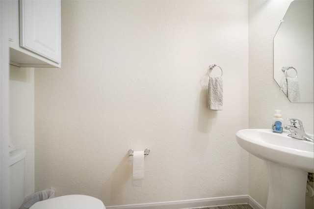 bathroom featuring toilet, a sink, baseboards, and wood finished floors