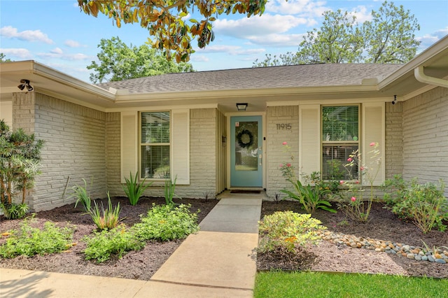 entrance to property featuring roof with shingles and brick siding