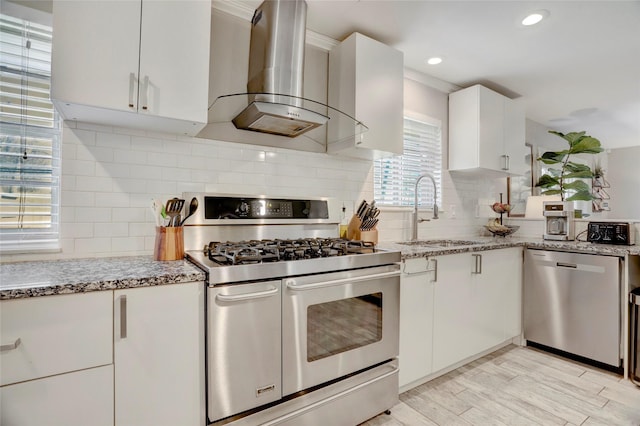 kitchen featuring stainless steel appliances, a sink, decorative backsplash, and wall chimney exhaust hood