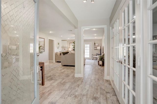 corridor with baseboards, french doors, and light wood-type flooring