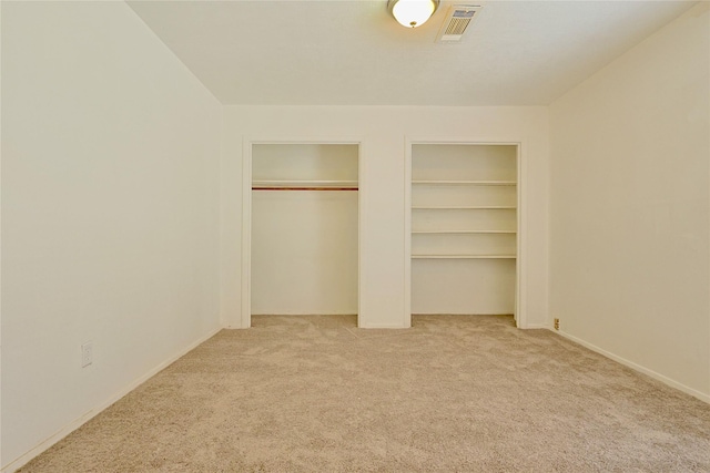 unfurnished bedroom with two closets, carpet, baseboards, and visible vents