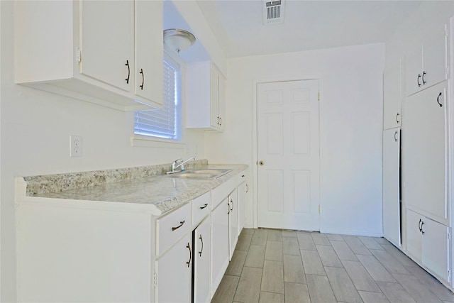 kitchen featuring a sink, white cabinetry, light countertops, and visible vents