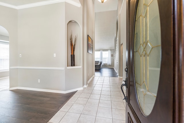 entrance foyer featuring arched walkways, baseboards, crown molding, and light tile patterned flooring