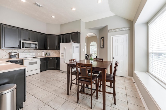 kitchen featuring white appliances, visible vents, decorative backsplash, arched walkways, and light countertops