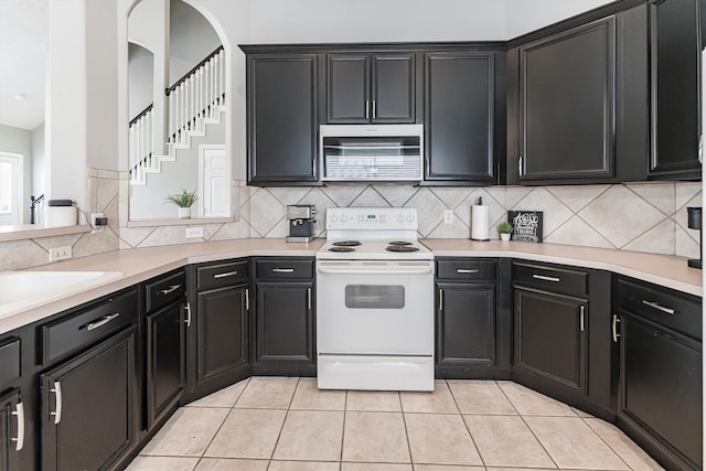 kitchen with stainless steel microwave, light countertops, white electric stove, and dark cabinets
