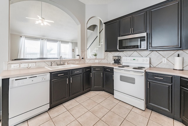 kitchen featuring dark cabinetry, white appliances, a sink, backsplash, and light countertops