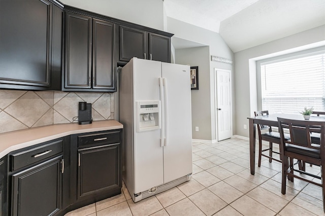 kitchen with white refrigerator with ice dispenser, lofted ceiling, light countertops, and dark cabinets