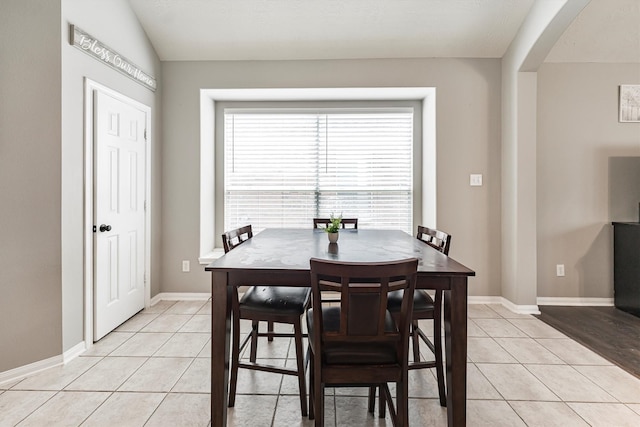 dining room with light tile patterned floors, baseboards, and arched walkways