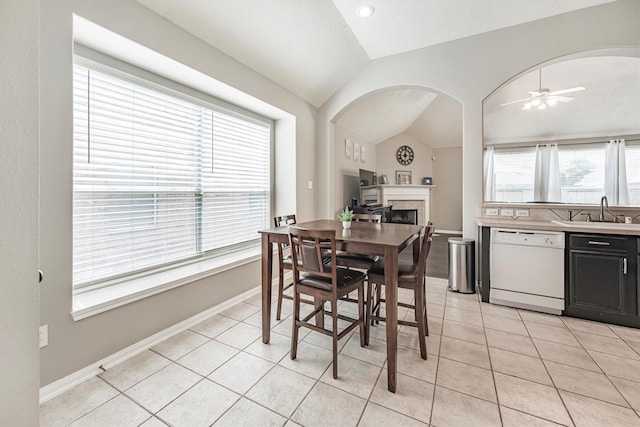dining space featuring light tile patterned flooring, vaulted ceiling, a fireplace, arched walkways, and a ceiling fan