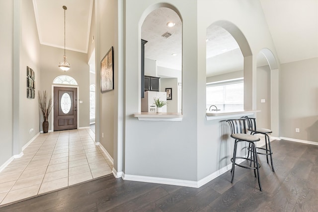 foyer entrance with baseboards, arched walkways, visible vents, and wood finished floors