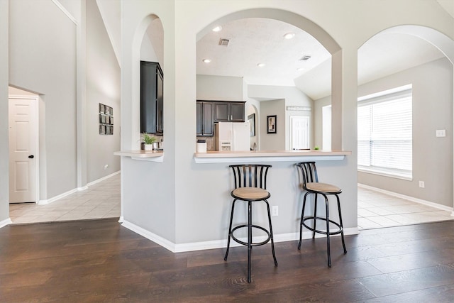 kitchen with light countertops, white fridge with ice dispenser, a breakfast bar area, and wood finished floors