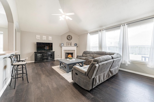 living room with lofted ceiling, ceiling fan, arched walkways, baseboards, and a tiled fireplace