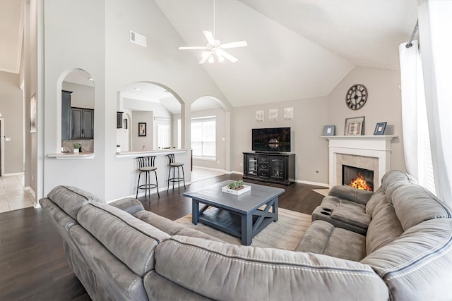 living room featuring wood finished floors, visible vents, arched walkways, a ceiling fan, and a tiled fireplace