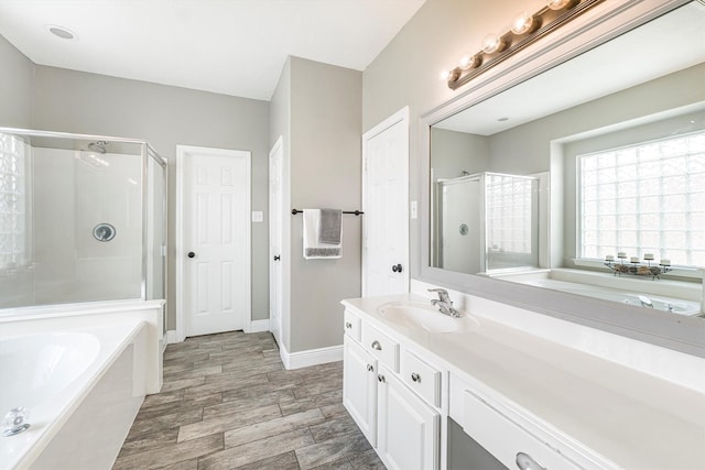 bathroom with a stall shower, vanity, a garden tub, and baseboards