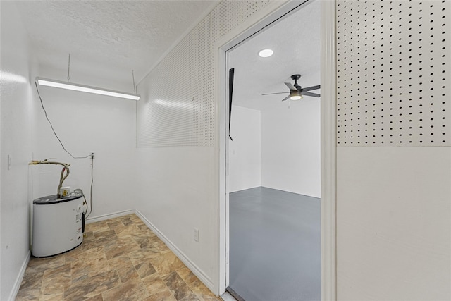clothes washing area with electric water heater, baseboards, a ceiling fan, and stone finish floor