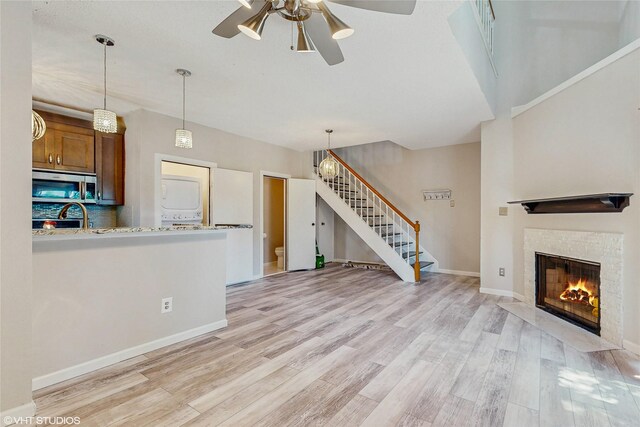 unfurnished living room featuring a ceiling fan, stacked washer / drying machine, a fireplace with flush hearth, light wood-type flooring, and stairs