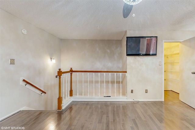 empty room with a textured ceiling, wood finished floors, baseboards, and ceiling fan
