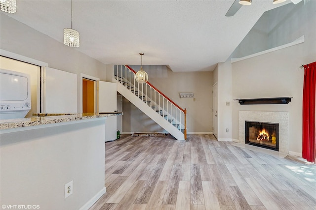 unfurnished living room featuring stairs, light wood finished floors, stacked washing maching and dryer, and a glass covered fireplace