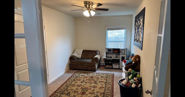 sitting room featuring carpet, baseboards, and a ceiling fan