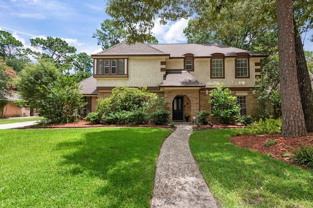 mediterranean / spanish house with stucco siding, brick siding, and a front lawn