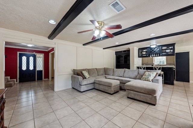 living room with light tile patterned floors, a decorative wall, visible vents, and a textured ceiling