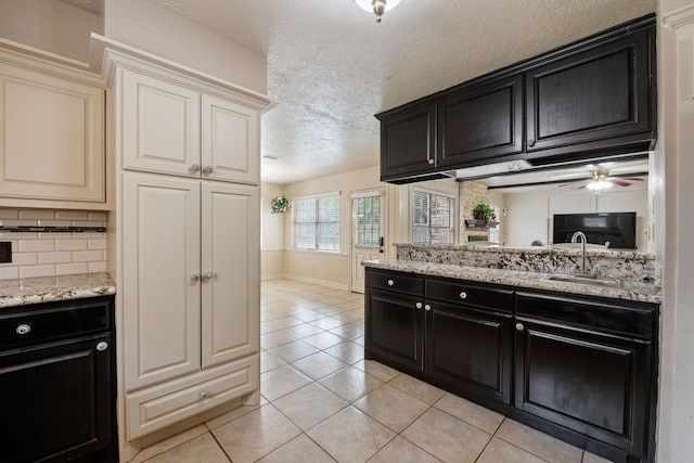 kitchen featuring a sink, a textured ceiling, decorative backsplash, dark cabinetry, and light tile patterned flooring