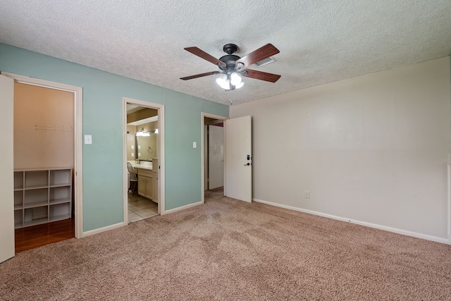 unfurnished bedroom with carpet, a textured ceiling, baseboards, ensuite bath, and a spacious closet