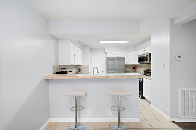 kitchen featuring a sink, a peninsula, stainless steel appliances, visible vents, and decorative backsplash