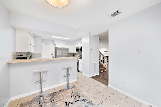 kitchen featuring a peninsula, tasteful backsplash, light tile patterned flooring, visible vents, and appliances with stainless steel finishes