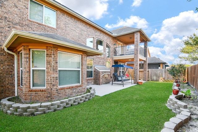 rear view of property with a balcony, a lawn, brick siding, a patio area, and a fenced backyard