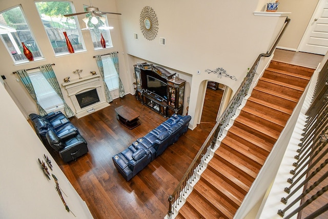 living room featuring wood finished floors, a high ceiling, a premium fireplace, ceiling fan, and stairs