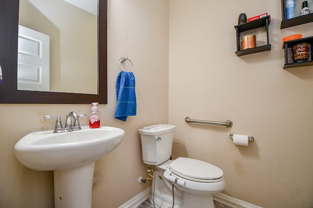 half bathroom with toilet, baseboards, and a sink