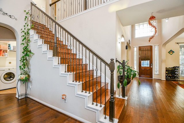 foyer entrance with stairs, washer / dryer, a towering ceiling, wood-type flooring, and arched walkways