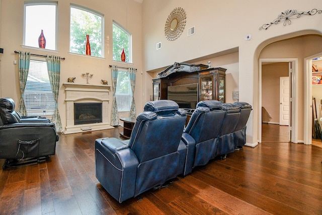 living area featuring a high ceiling, visible vents, dark wood-style flooring, arched walkways, and a fireplace with raised hearth
