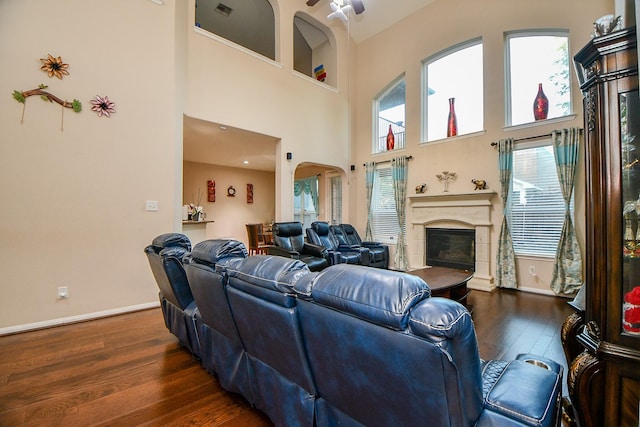 living room with a towering ceiling, arched walkways, dark wood-style floors, baseboards, and a glass covered fireplace