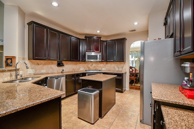kitchen featuring a sink, tasteful backsplash, light stone counters, and appliances with stainless steel finishes
