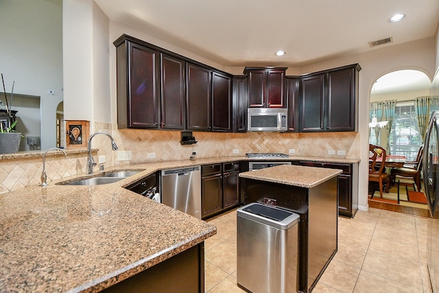 kitchen with a sink, arched walkways, light stone counters, and appliances with stainless steel finishes