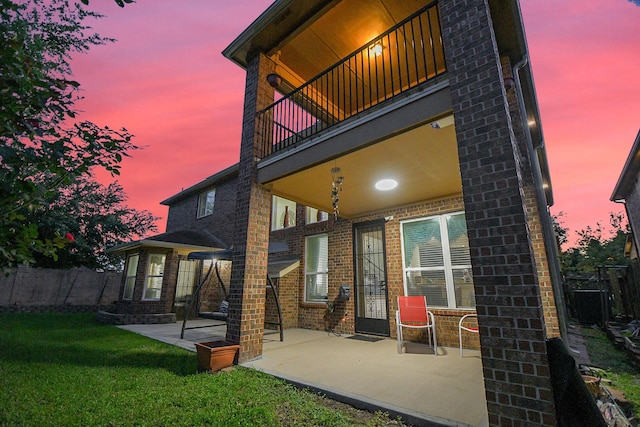 back of house with fence, brick siding, a balcony, a yard, and a patio