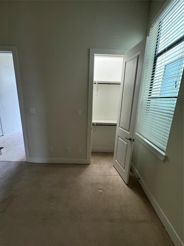 unfurnished bedroom with carpet flooring, a closet, baseboards, and a walk in closet