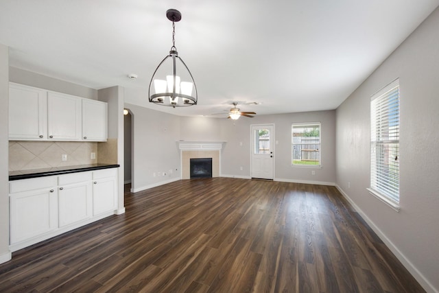 15319 Sableton Crest Ln, Cypress, TX 77429 - unfurnished living room featuring baseboards, dark wood-style flooring, a tiled fireplace, and ceiling fan with notable chandelier