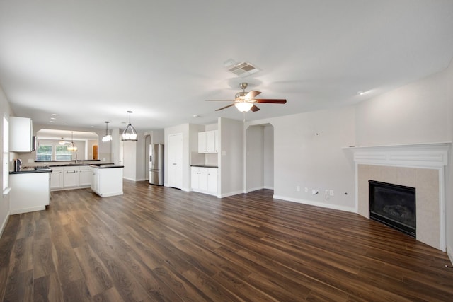 15319 Sableton Crest Ln, Cypress, TX 77429 - unfurnished living room featuring baseboards, a tiled fireplace, visible vents, ceiling fan with notable chandelier, and dark wood-type flooring
