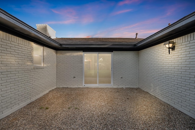 213 Westview Dr, Sealy, TX 77474 - exterior entry at dusk with brick siding, a chimney, a shingled roof, and a patio area