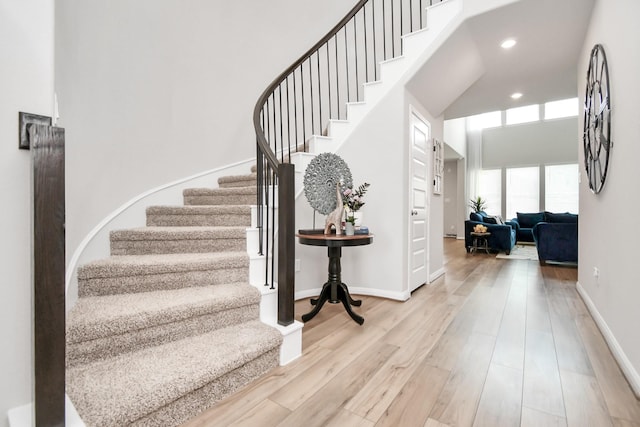 stairs featuring wood finished floors, baseboards, a high ceiling, and recessed lighting