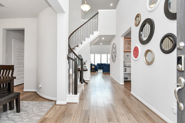 foyer entrance featuring wood finished floors, visible vents, baseboards, a towering ceiling, and stairs