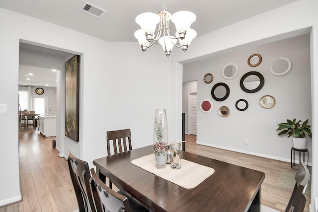 dining space featuring an inviting chandelier, baseboards, visible vents, and light wood-style floors
