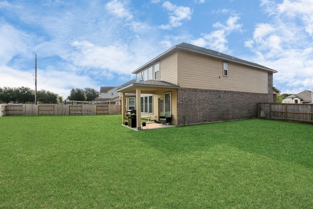 rear view of house with a yard, a patio, brick siding, and a fenced backyard