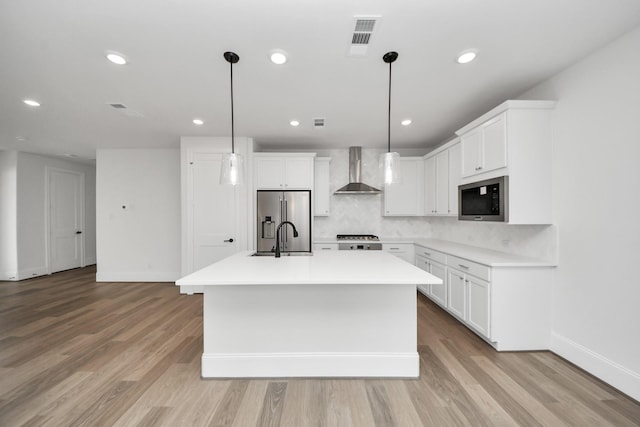 kitchen with built in microwave, wall chimney exhaust hood, stainless steel refrigerator with ice dispenser, a kitchen island with sink, and baseboards