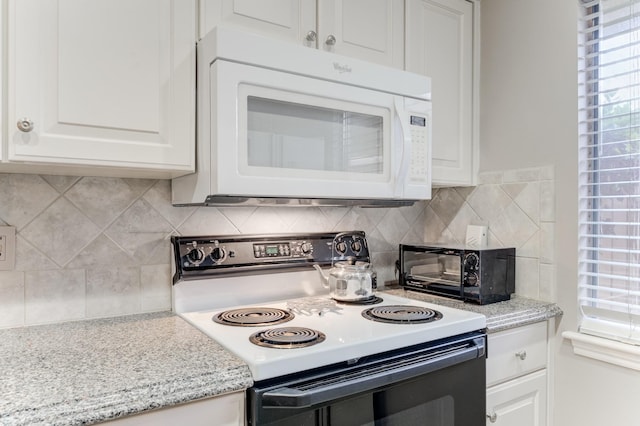 kitchen with white microwave, a toaster, decorative backsplash, white cabinets, and electric stove